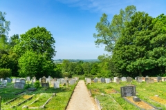 A rolling countryside view from the rear of the church. Gravestones and a path can be viewed in the foreground.